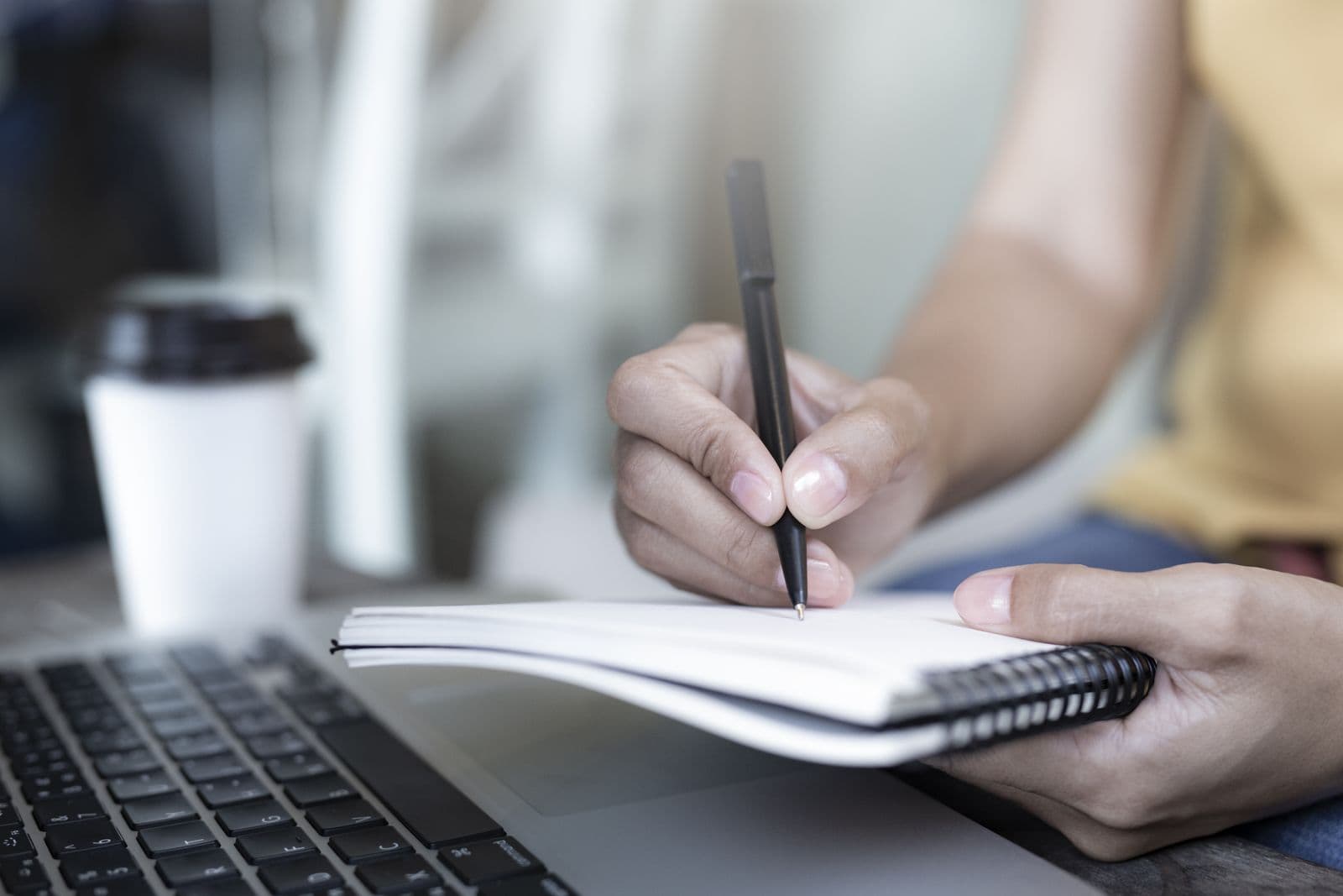 Student piše beleške za diplomski rad pored laptopa