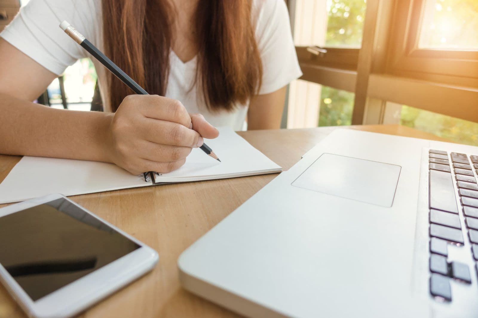 Studentkinja piše plan diplomskog rada u svesci pored laptopa